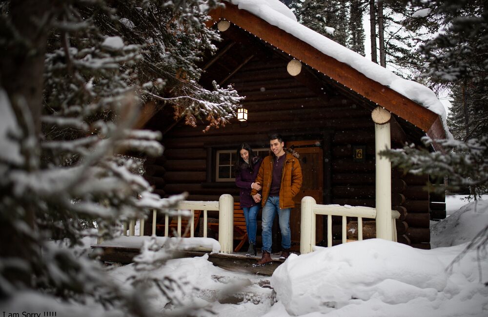 A couple walking out of a snowy cabin at Storm Mountain Lodge and Cabins in the winter in Banff National Park.